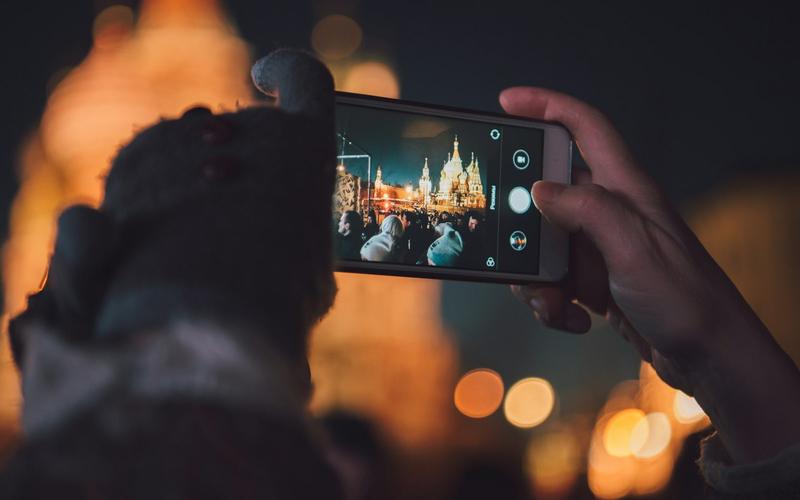 A hand holding a phone, framing a photograph of a lit building at night